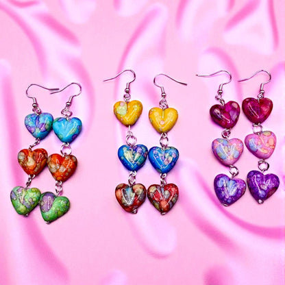 Colorful heart-shaped earrings on a pink fabric background