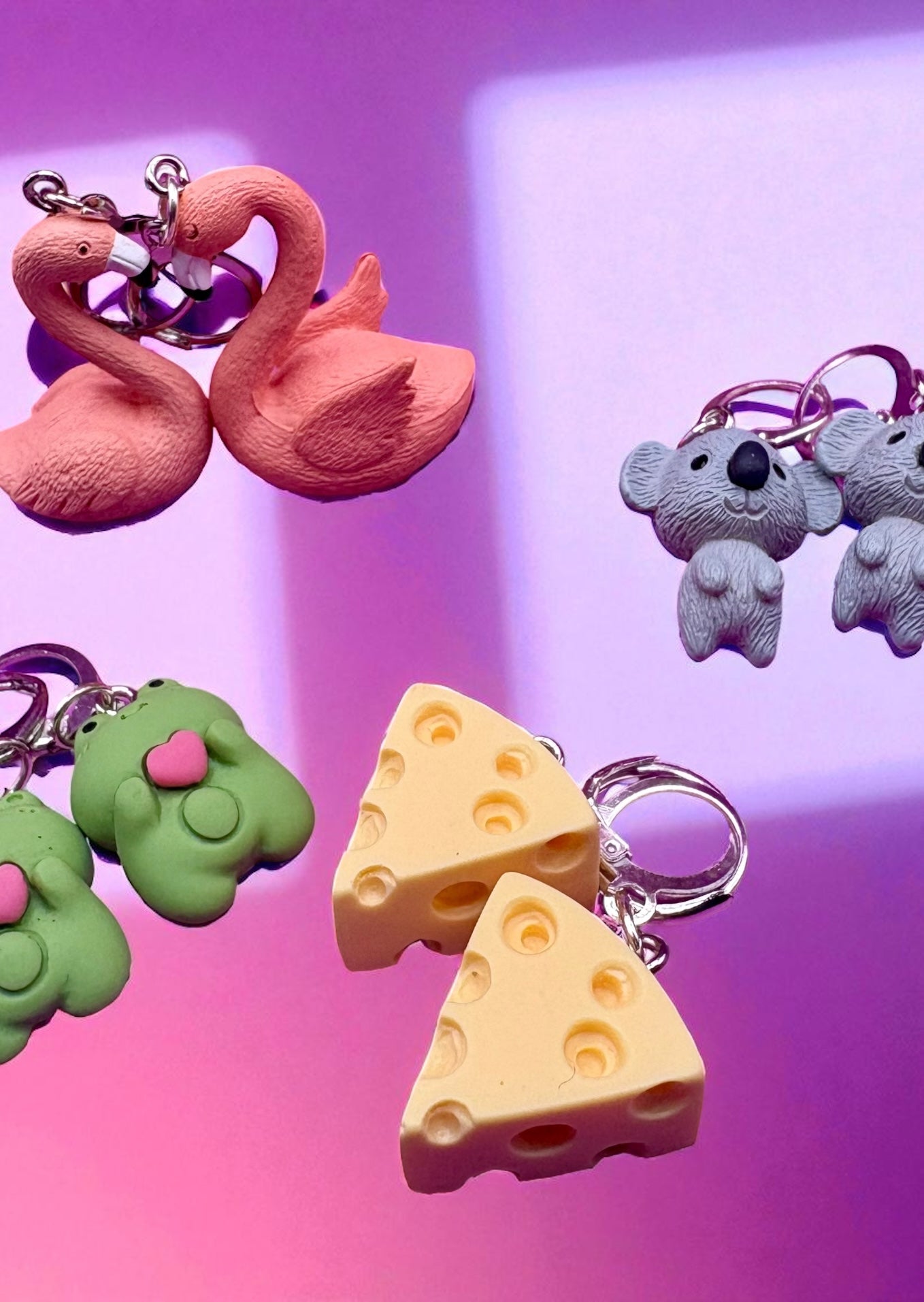 Colorful keychains including a pink swan, green creature, purple flower, and cheese slices on a gradient background.