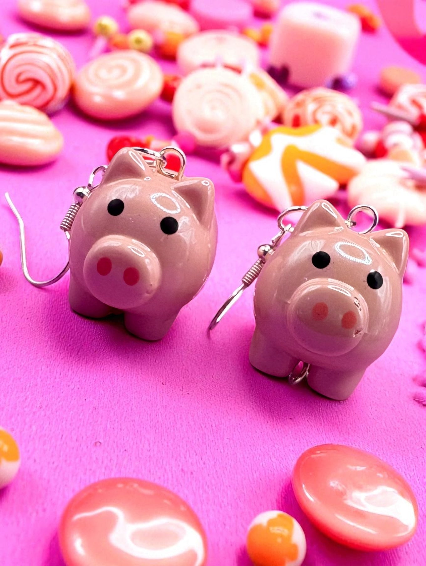 Pink piggy  earrings on a pink background with colorful candies.