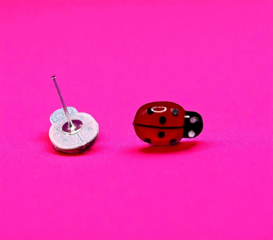 Two toy cars, one resembling a ladybug and the other a silver car with a wheel, on a pink background.