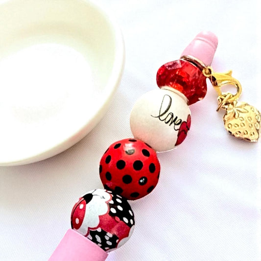 Beaded pen with ladybug design and 'love' charm on a white background