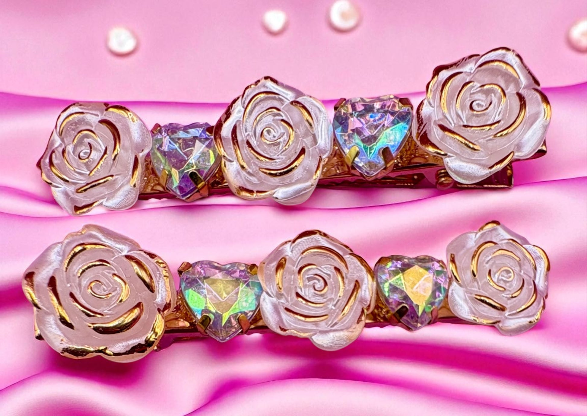 Two decorative hair clips with rose and heart designs on a pink satin background