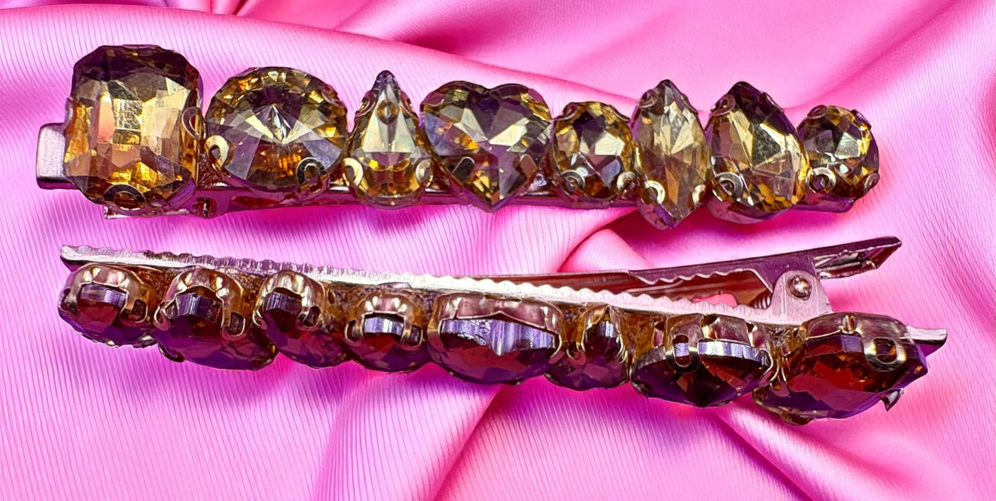 Two decorative hair clips with gemstones on a pink satin background