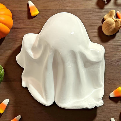 White ghost-shaped plate on a wooden surface with Halloween decorations.