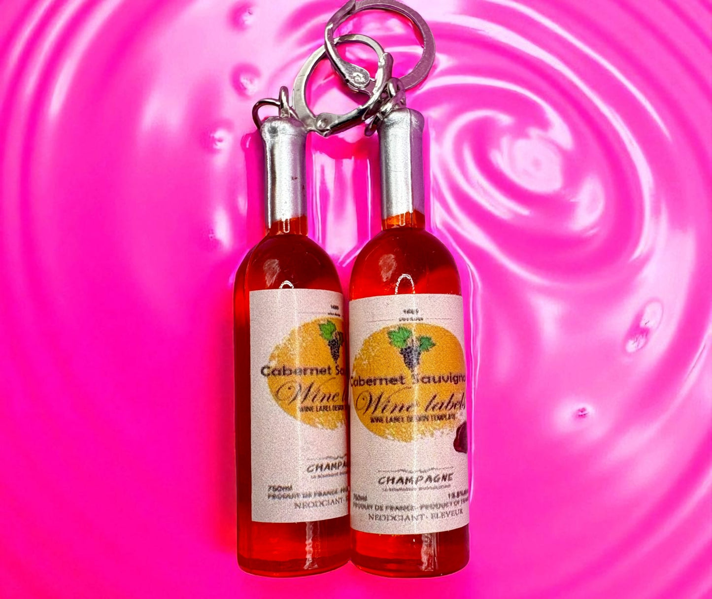 Two miniature wine bottle  earrings on a pink swirling background