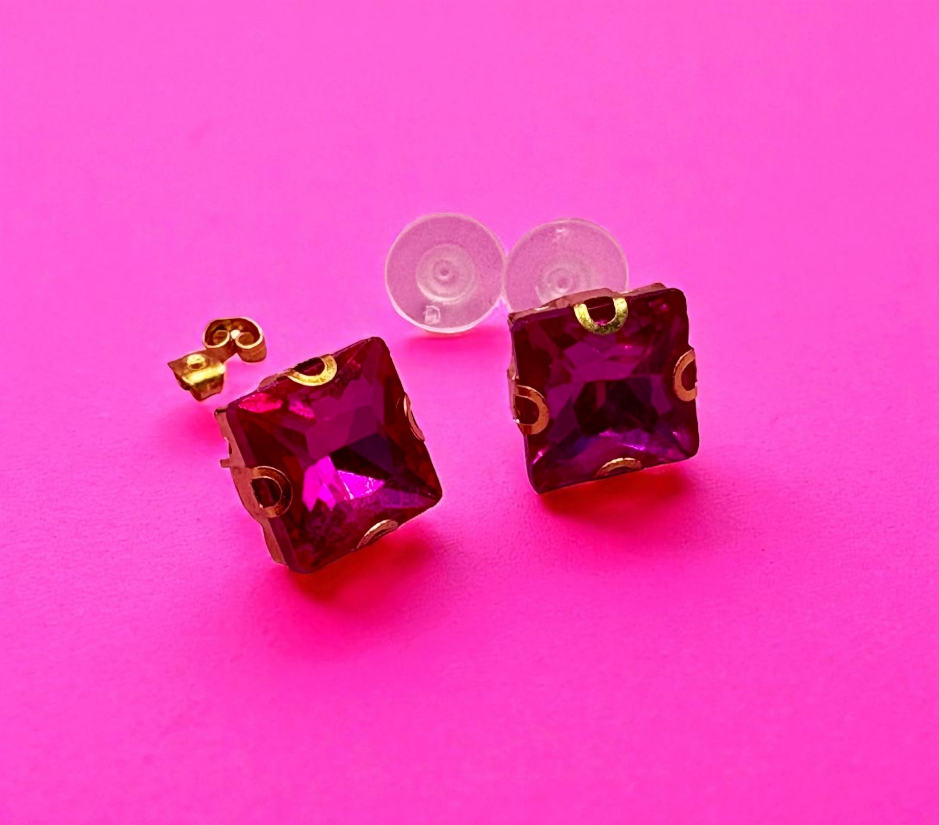 Amethyst-colored square stud earrings on a pink background