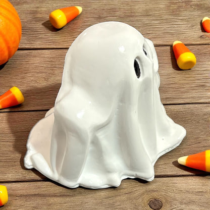 White ghost-shaped figure on a wooden surface with candy corn and a pumpkin.