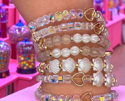 Stack of colorful beaded bracelets on a person's wrist with a pink background.