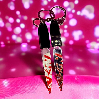 Pair of knife-shaped earrings with red and white design on a pink background