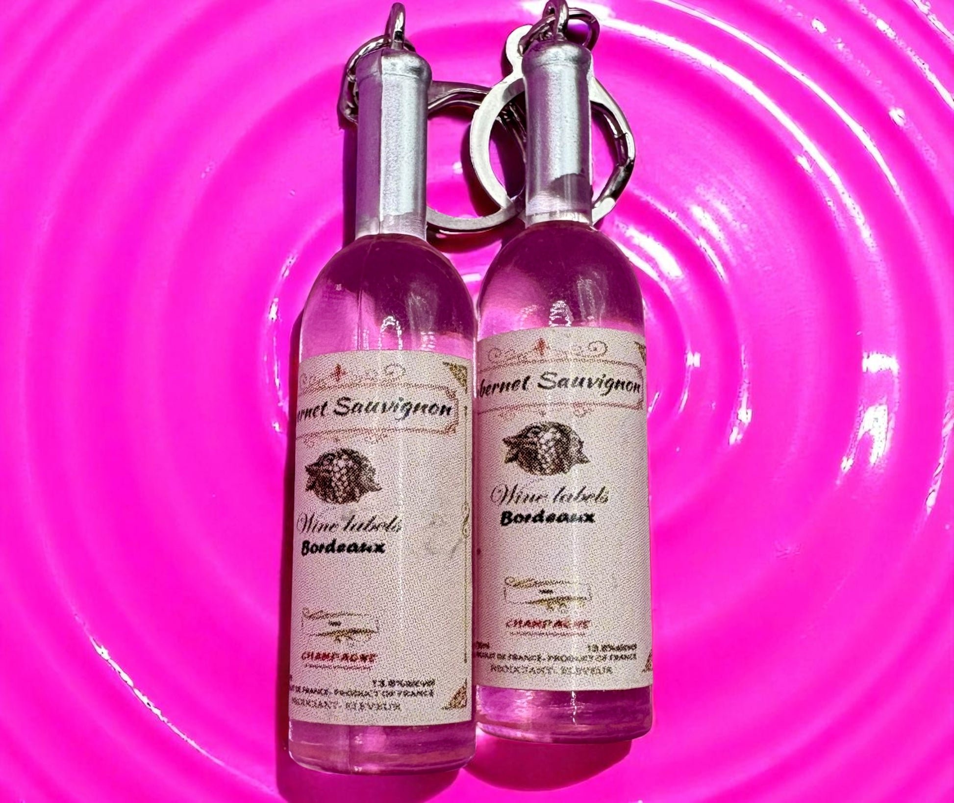 Two pink wine bottle  earrings with labels on a pink circular background