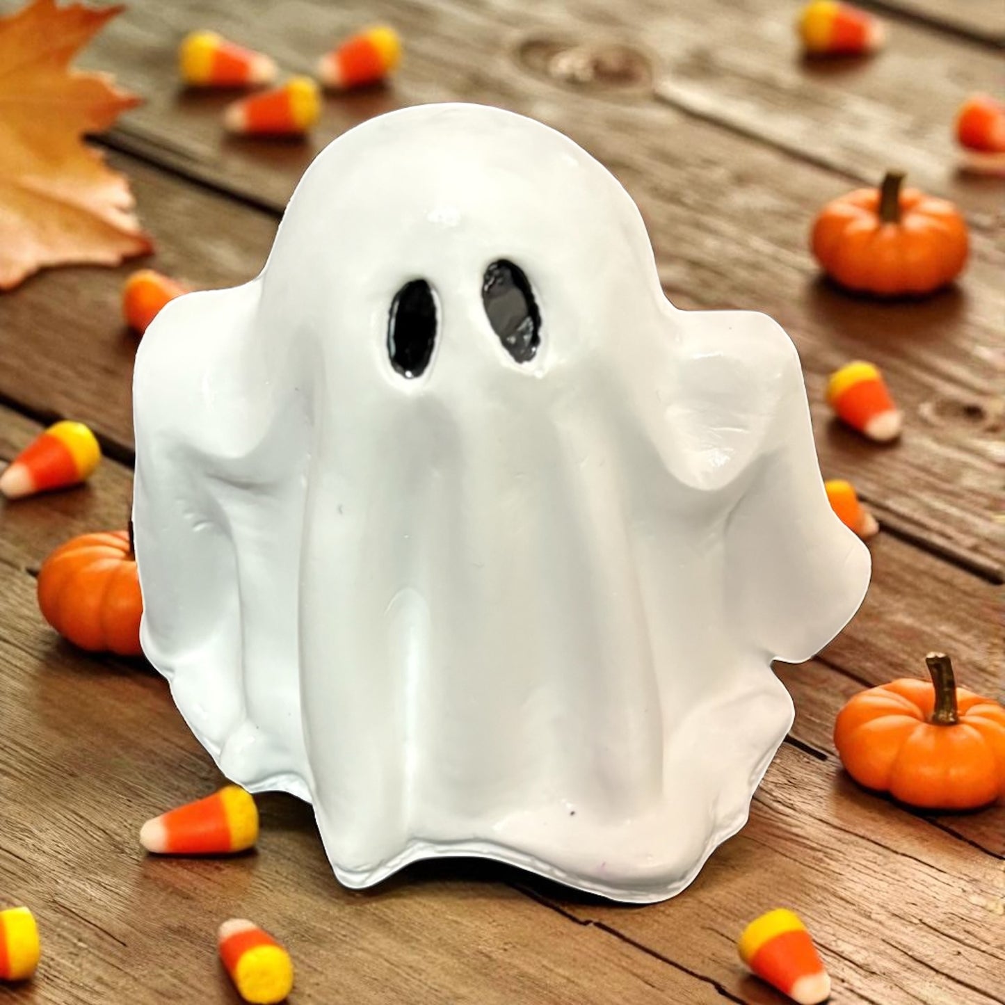 Halloween-themed ghost decoration on a wooden surface with pumpkins and candy corn.