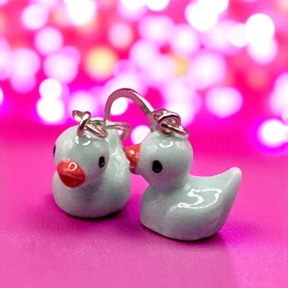 Pair of duck-shaped earrings on a pink background with bokeh effect