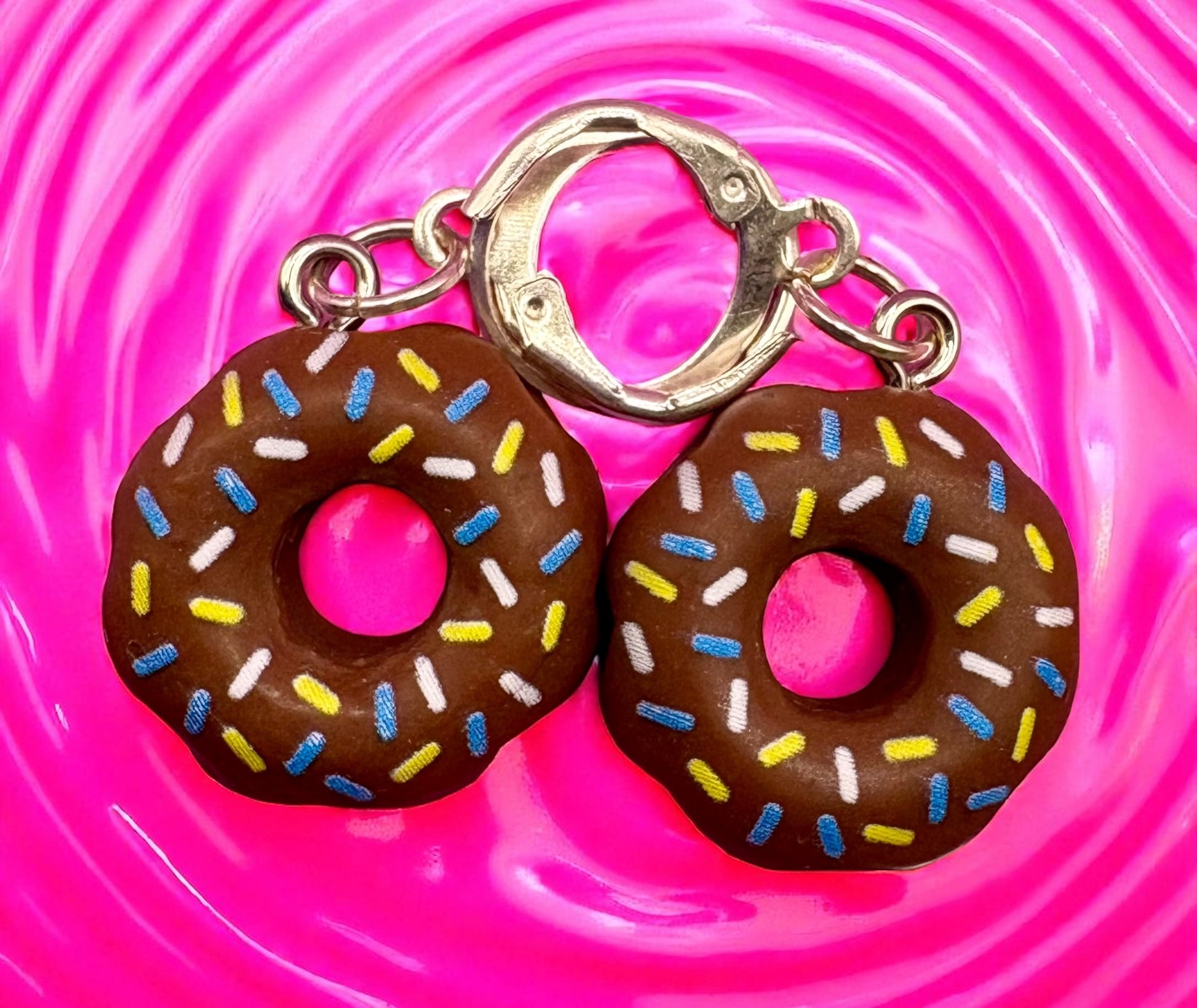 Donut-shaped  earrings with colorful sprinkles on a pink swirling background