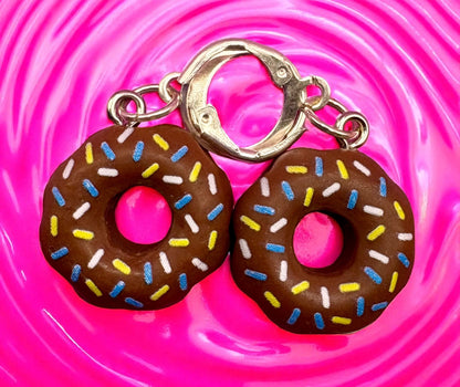 Donut-shaped  earrings with colorful sprinkles on a pink swirling background