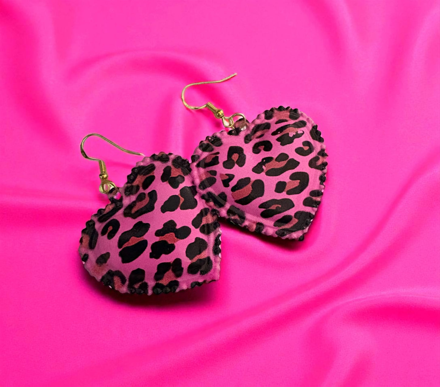 Heart-shaped earrings with leopard print design on a pink satin background