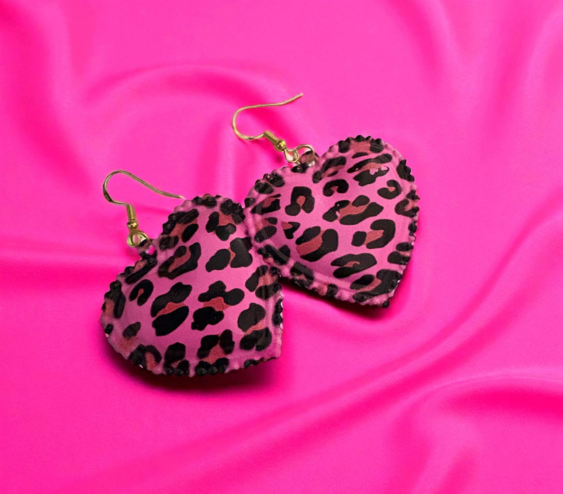 Heart-shaped earrings with leopard print design on a pink satin background