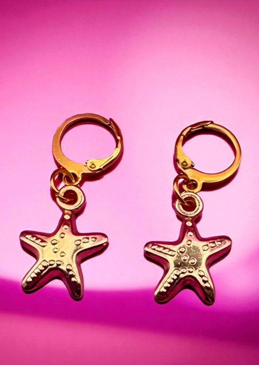 Gold starfish-shaped earrings on a pink background