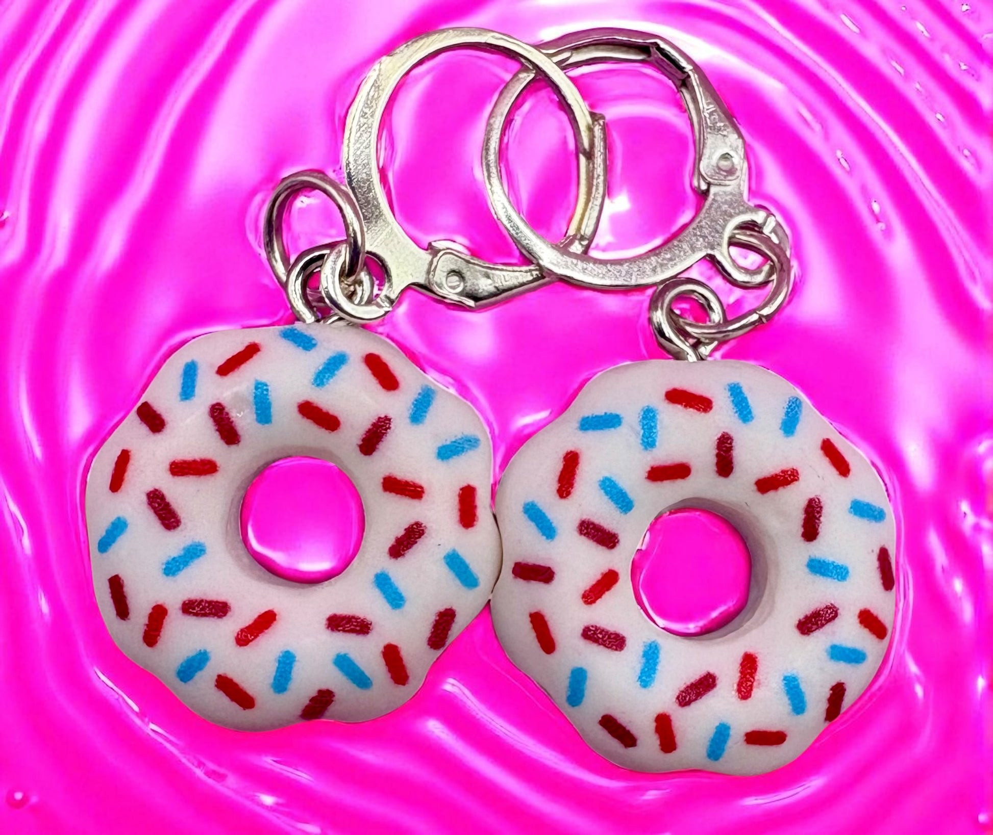Donut-shaped  earrings with colorful sprinkles on a pink background