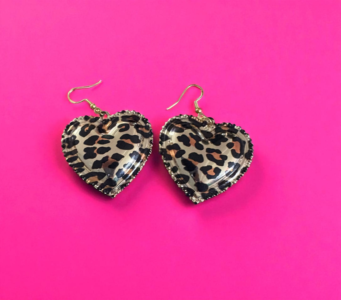 Heart-shaped leopard print earrings on a pink background