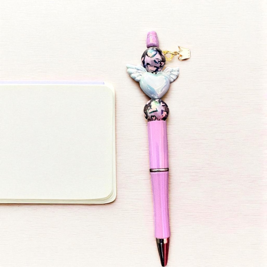 Pink pen with angel charm on a light pink background