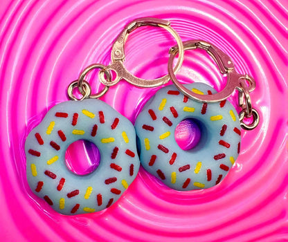 Two donut-shaped earrings with colorful sprinkles on a pink background