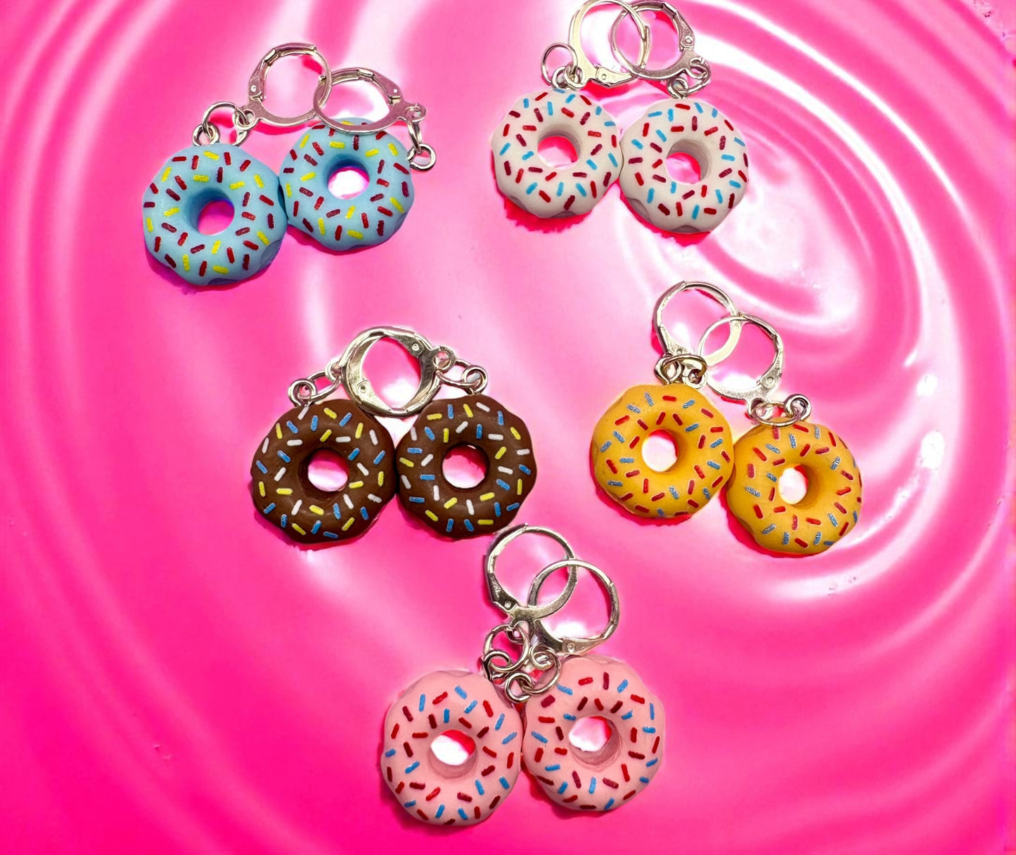 Set of colorful donut-shaped earrings on a pink water surface