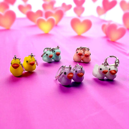 Colorful duck-shaped keychains on a pink background with heart shapes.