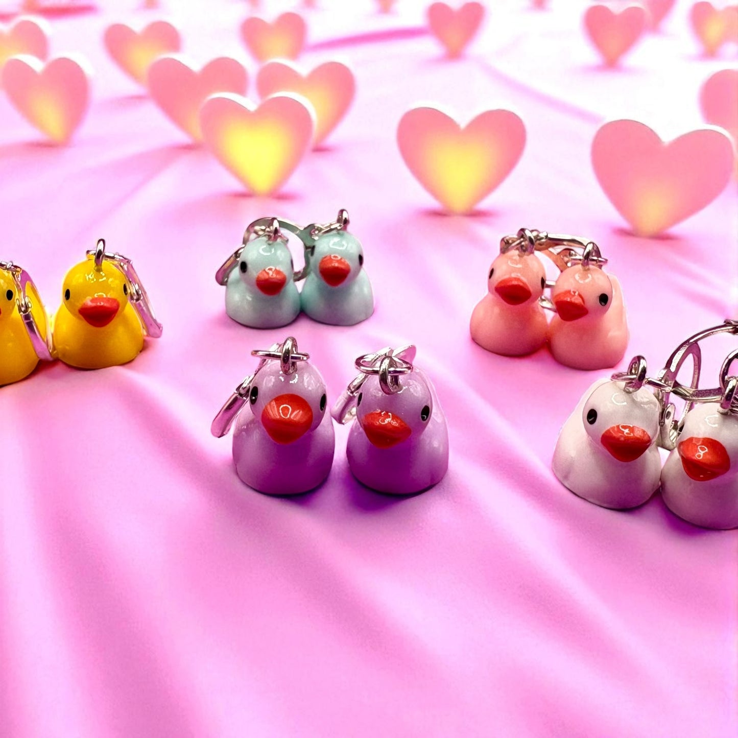 Set of colorful duck-shaped keychains on a pink background with heart shapes.