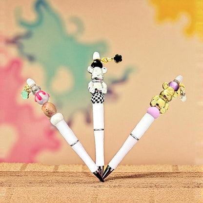 Four decorative pens with colorful bead attachments on a wooden surface.