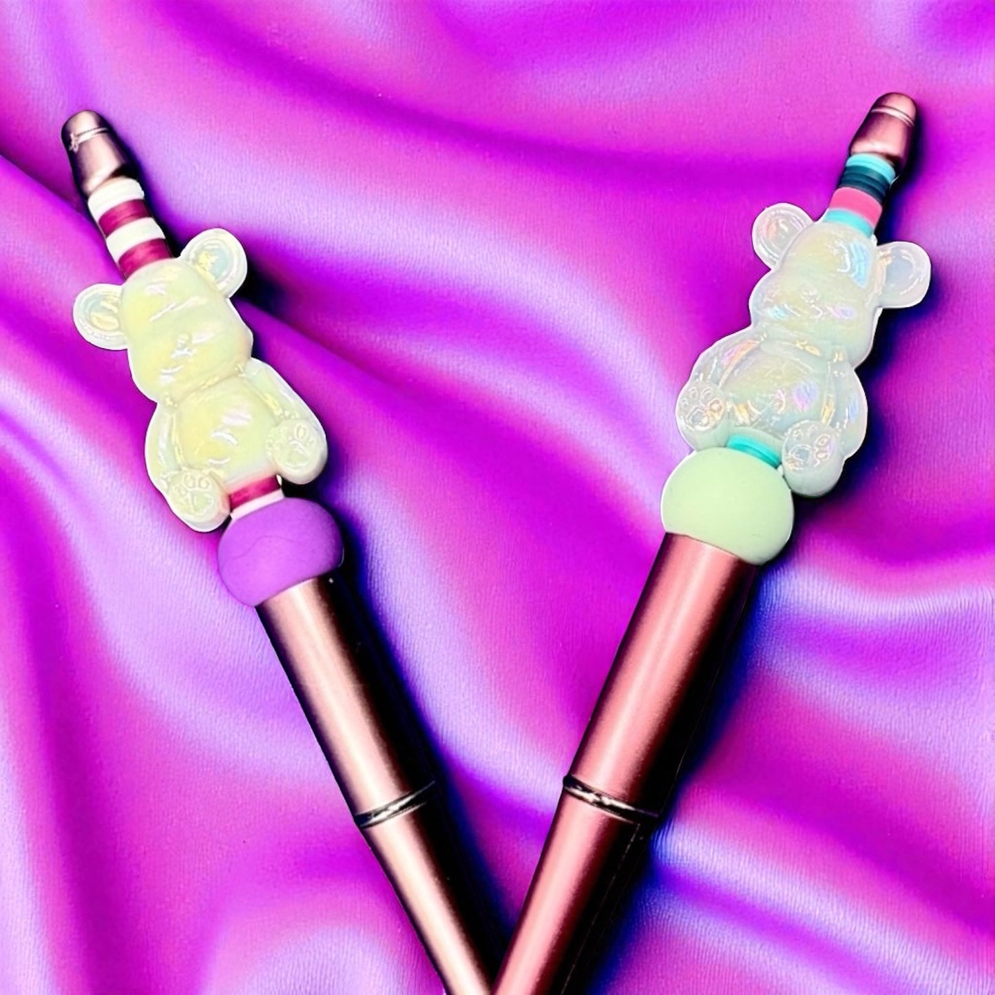 Two colorful pen tips with bear-shaped ends on a vibrant purple background