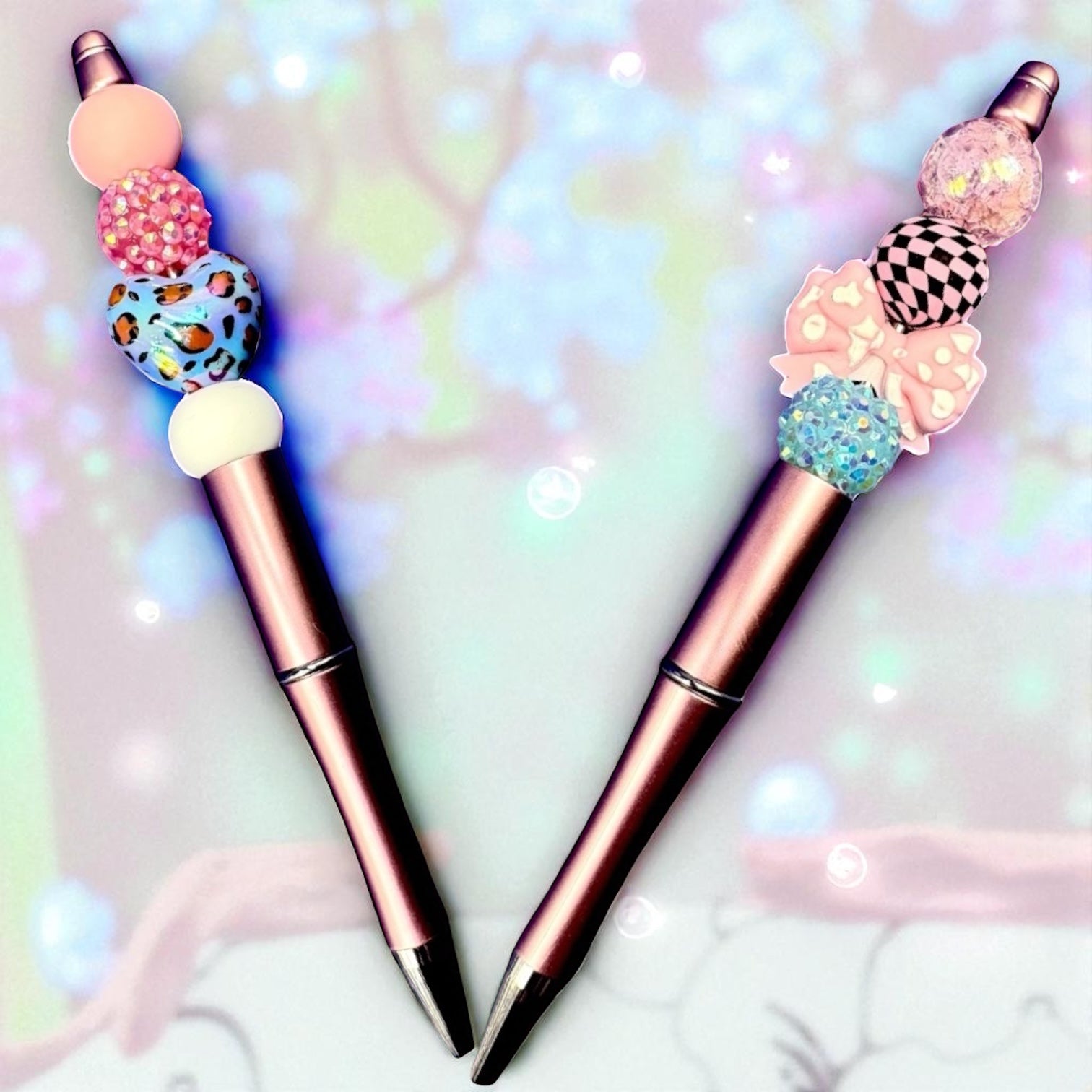 Two decorative pens with colorful bead caps on a soft, blurred background.