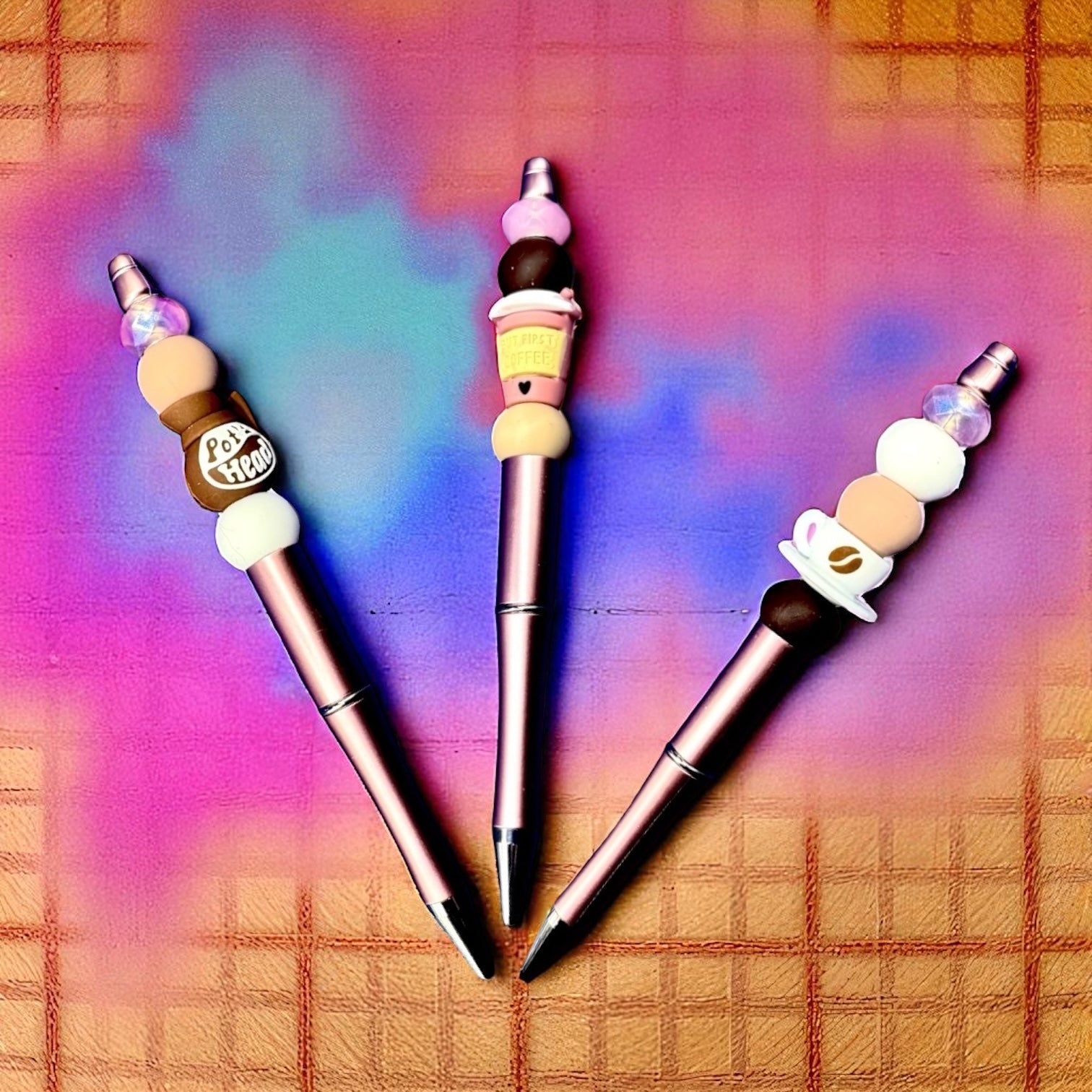 Three decorative pens with colorful bead accents on a plaid background