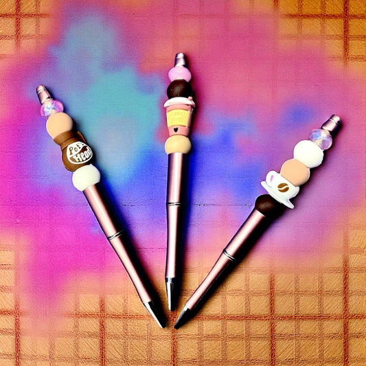 Three decorative pens with colorful bead accents on a plaid background