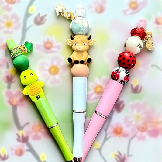 Three colorful pens with animal-themed charms on a floral background