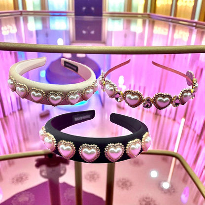 Three headbands with heart-shaped pearl decorations on a reflective surface.